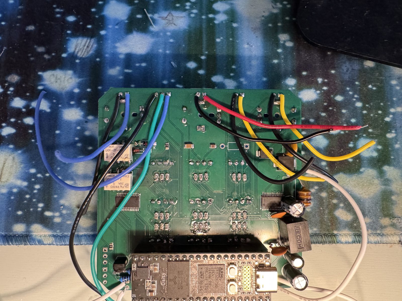 A green circuit board on a starry desk mat, a Daisy Seed along its bottom edge, wires in blue, green, red, yellow and white soldered to it