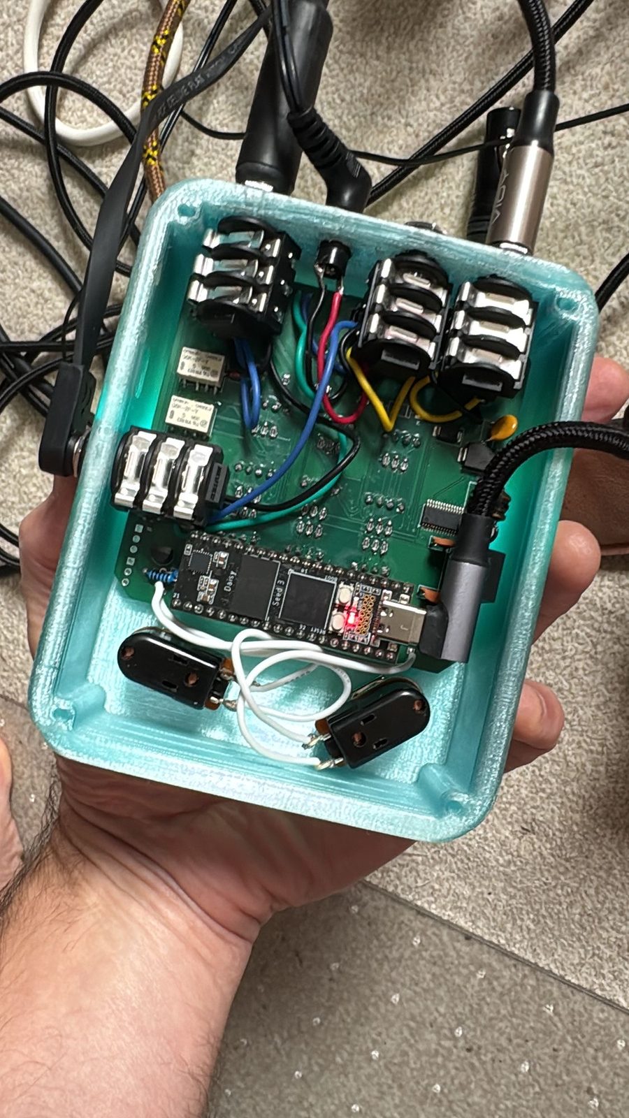 Inside a pale teal moonstone held open in a hand: the jacks along the top, a green circuit board with a Daisy Seed across it, and the two footswitches at the bottom, wired in white