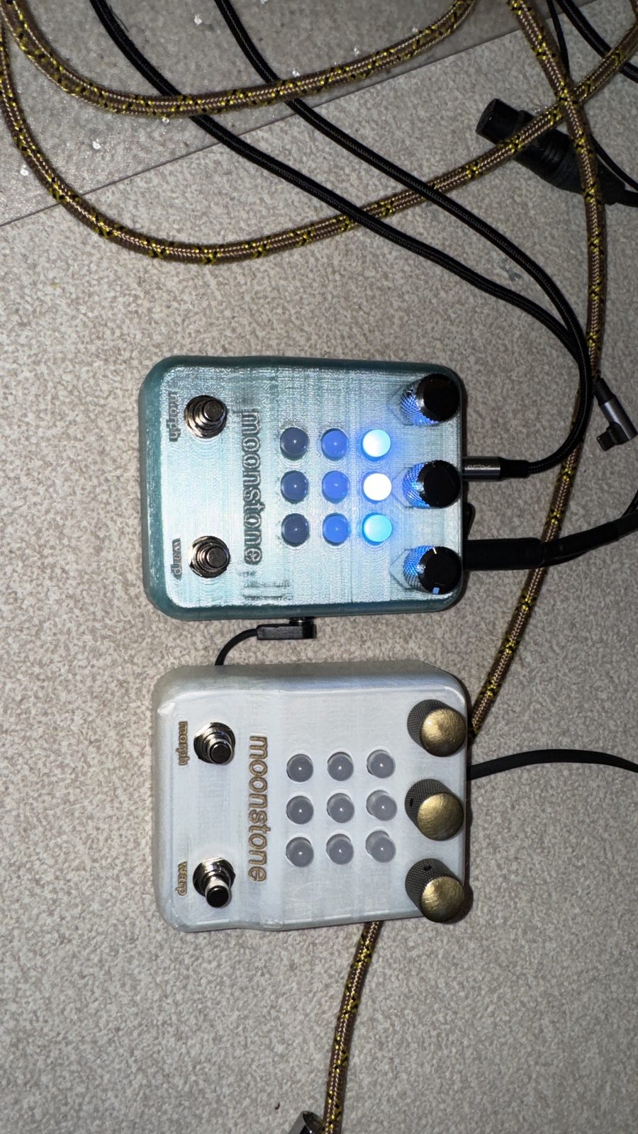 Two moonstones side by side on a carpet: one pale teal with black knobs and blue lights, one white with brass knobs