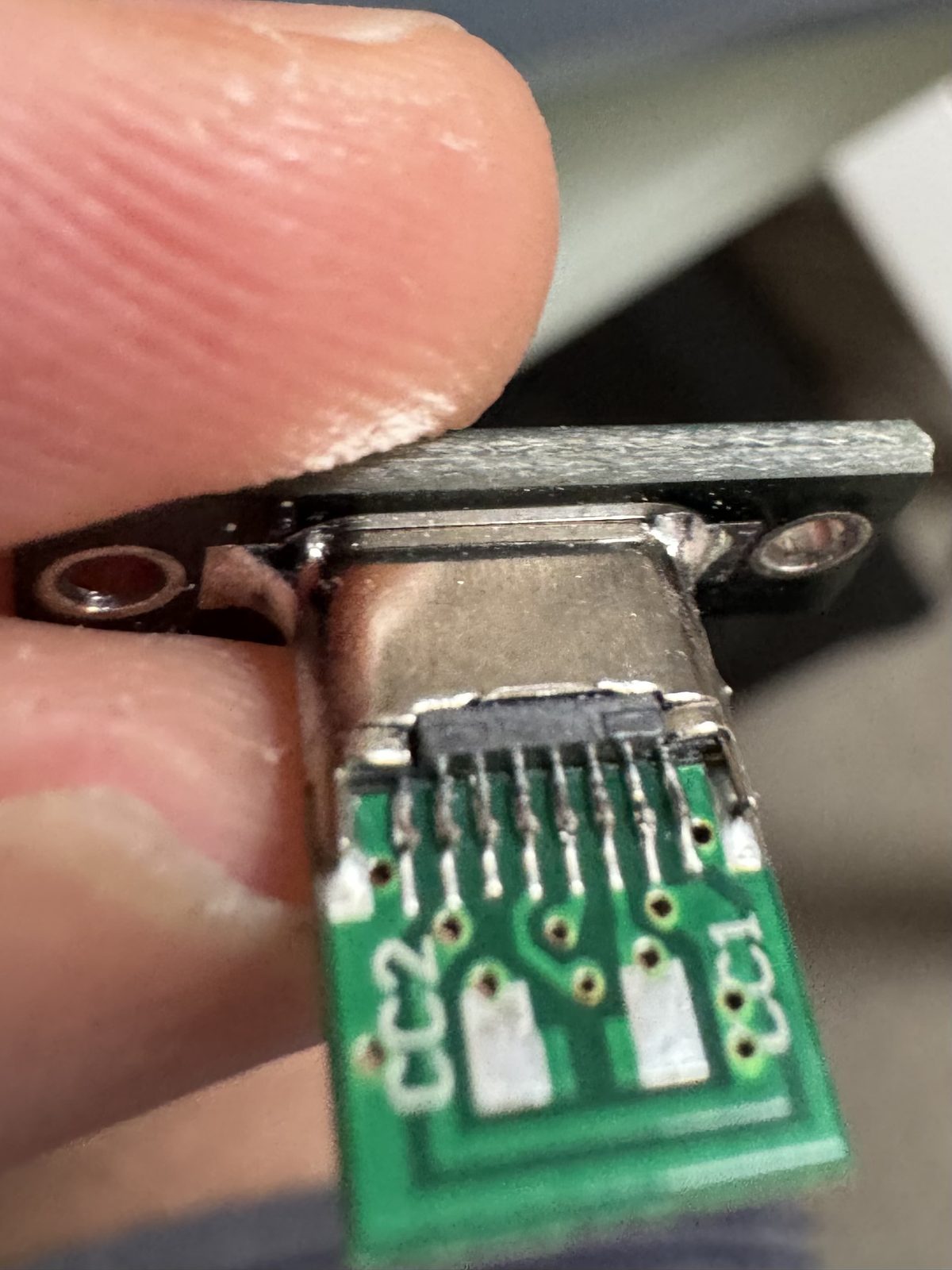 A small green board with a USB-C socket on it, held between two fingers, its CC1 and CC2 pads showing